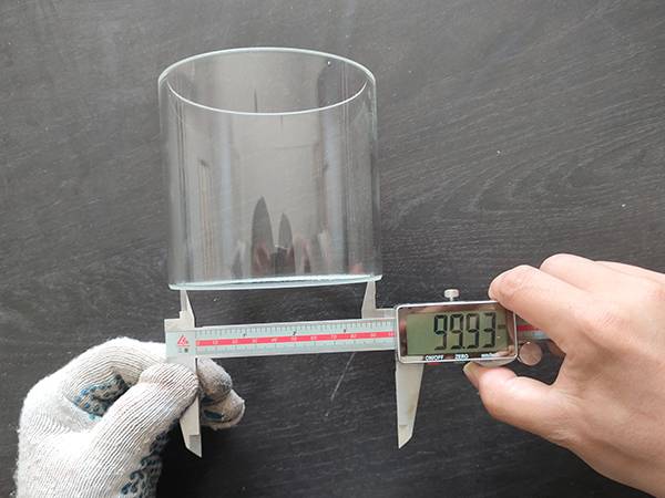 A worker is measuring the precision glass cylinder diameter.